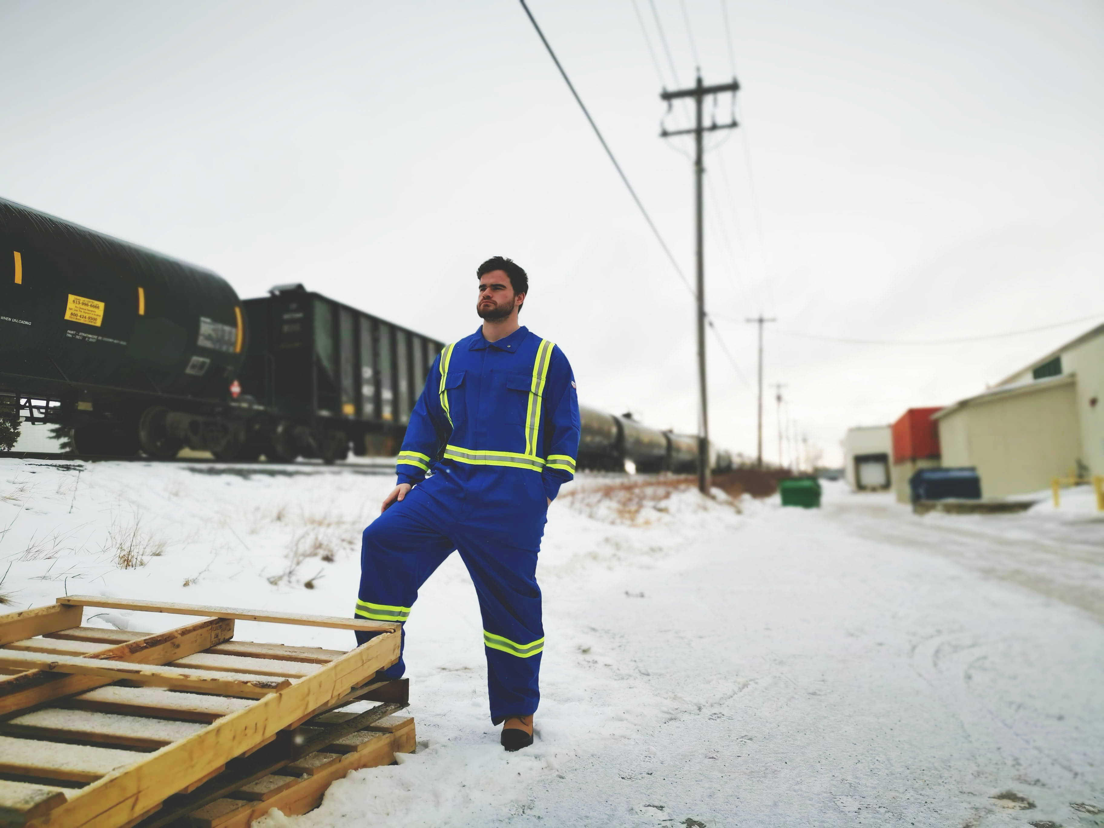 Man in royal blue hi viz striped coveralls stands near a rail yard