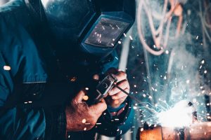 Person in full welding mask uses tools to weld metal together